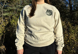 Person wearing a cream crewneck with a green logo outdoors