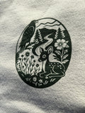 Black and green illustration of a deer and eagle in a circular design on a cream sweater.