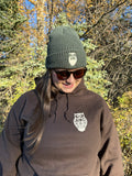 Person wearing a brown hoodie with a logo and a green beanie outdoors.
